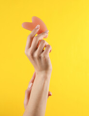 Woman's hand holds a massage jade gua sha on a yellow background. Anti-aging therapy