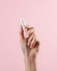 Woman's hand holds a tampon on pink background. Feminine hygiene, menstruation, critical days