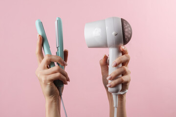 Fashionable modern hair dryer and hair straightener in female hands on a pink background. Hair style