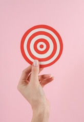 Target in a female hand on a pink background. Business concept. Achievements of goals