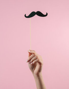 Gentleman's mustache of a photo booth party in a female hand on a pink background