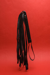 Leather sex whip levitating on red background. Dominance. Sex games. Floating Objects