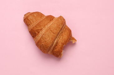 Appetizing bitten croissant on a pink background