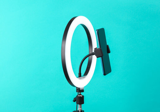 Led ring lamp with smartphone on tripod, blue background. Vlogging, beauty blog