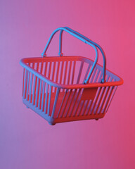 Supermarket basket floating in the air, isolated in blue-red neon gradient light. Levitating objects. Minimal concept