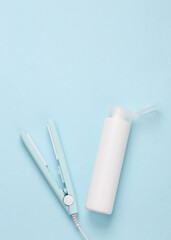 Mini hair straightener with a bottle of shampoo on a blue background. Hair style. Top view