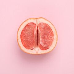 Gynecology, female intimate hygiene. Half of a ripe grapefruit symbolizing the female vagina on a pink background. Creative idea, allegory, fresh idea. Top view - obrazy, fototapety, plakaty