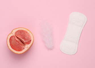 Gynecology, female intimate hygiene, menstruation. Half of grapefruit symbolizing female vagina with pads, feathers on pink background. Top view