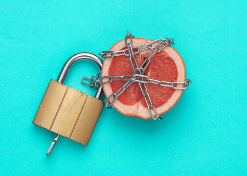 Loyalty concept. A grapefruit half, symbolizing the vagina, wrapped in a steel chain with a lock. Blue background. Creative idea