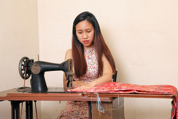Young Asian woman using tailoring cloth fabric on a retro vintage old sewing machine