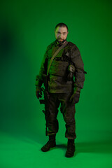 soldier in the studio on a green background with colored light. a man in military uniform with a gun, rifle or machine gun. military. airball player
