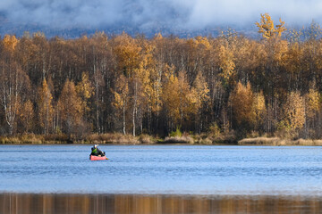 An angler in a bright red canoe on a sunny autumn day in Alaska.