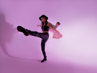 Stylish young woman in a black hat and jacket. posing in the studio with pink light on the background