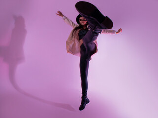 Stylish young woman in a black hat and jacket. posing in the studio with pink light on the...