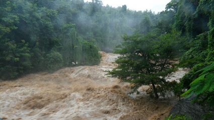 Waterfall cataract in forest mountains. Dirty streams are flowing down the mountain slopes of the mountain forest after heavy rains in Thailand. River flood, selective focus.