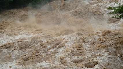 Waterfall cataract in forest mountains. Dirty streams are flowing down the mountain slopes of the mountain forest after heavy rains in Thailand. River flood, selective focus.