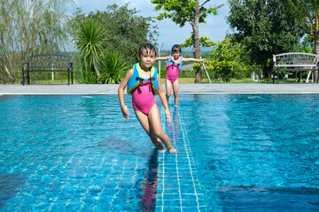 Naklejka premium Happy little sisters play in outdoor swimming pool of tropical resort during family summer vacation. Kids learning to swim. Healthy Summer Activities for Kids.