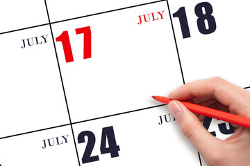 A hand holding a red pen and pointing on the calendar date July 17. Red calendar date, copy space,...