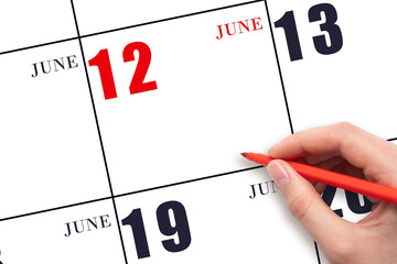 A hand holding a red pen and pointing on the calendar date June 12. Red calendar date, copy space,...
