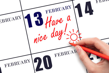 The hand writing the text Have a nice day and drawing the sun on the calendar date February 13