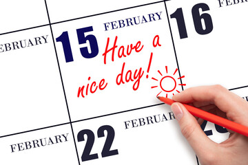 The hand writing the text Have a nice day and drawing the sun on the calendar date February 15