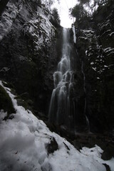 burgbach waterfall idyllically located in the forest between trees. Snowy landscape in winter from the German Black Forest