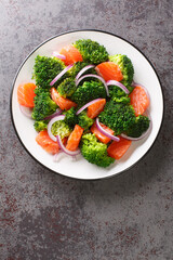 Dietary salad of steamed broccoli, salted salmon and red onion close-up in a plate on the table. Vertical top view from above