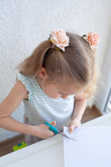The girl cuts and sculpts from plasticine, is engaged in creativity at a white table against a...