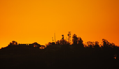 Telecommunication scafolding tower with internet data voice and GSM antennas photographed on top of a hill against amazing orange sunrise sky. Communication technology industry mixed with nature.