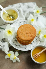 Fototapeta na wymiar Honey cookies with natural patterns on a plate on a dinner table with flowers and tea. Food photography in light colors with cookies and spring daffodils.