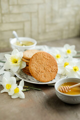 Obraz na płótnie Canvas Honey cookies with natural patterns on a plate on a dinner table with flowers and tea. Food photography in light colors with cookies and spring daffodils.