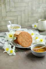 Honey cookies with natural patterns on a plate on a dinner table with flowers and tea. Food photography in light colors with cookies and spring daffodils.