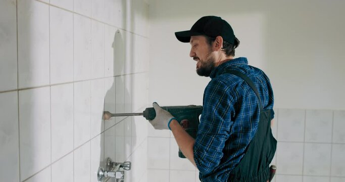 Detail view of a construction worker using a handheld demolition hammer and wall breaker to chip away and remove old floor tiles during renovation work.