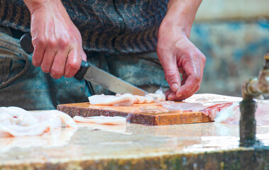 A pair of hands, with a sharp knife, slicing a fresh whole squid calamari,