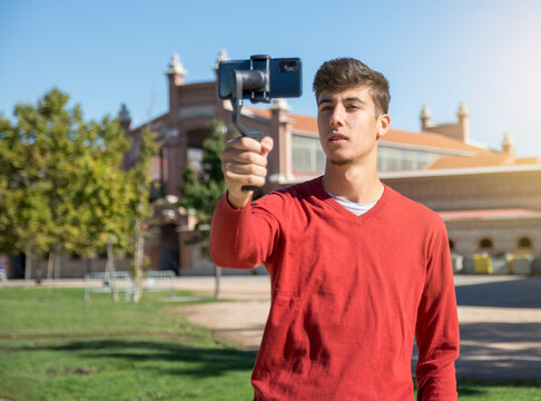 Portrait of businessman recording video presentation at smartphone with steadycam. Focused young man standing outside, holding steadycam while recording video presentation about new object 