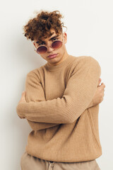 vertical photo of a handsome, handsome man standing on a light background, wearing beige clothes and sunglasses, looking at the camera with his arms folded on his chest