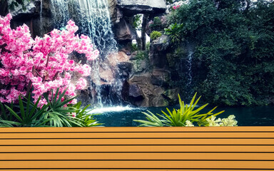 Brown table wooden shelf with pink flowers and waterfall backdrop.