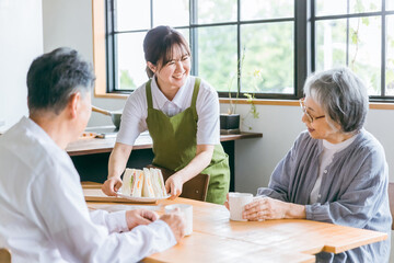 高齢者夫婦に食事を運ぶ介護福祉士の日本人女性
