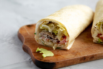 Homemade BLT tomato lettuce bacon Wrap with Mayo on a wooden board on a gray background, side view.