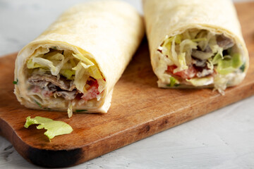 Homemade BLT tomato lettuce bacon Wrap with Mayo on a wooden board on a gray background, side view. Close-up.