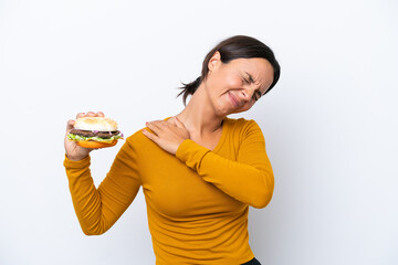 Young hispanic woman holding a burger isolated on white background suffering from pain in shoulder for having made an effort