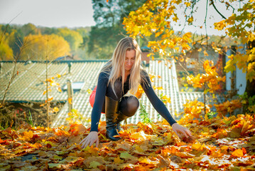 Portrait of a beautiful blonde in a red short skirt collecting yellow foliage in the autumn park.