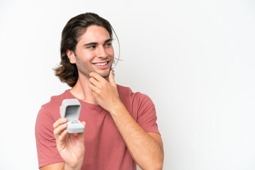 Young handsome man holding a engagement ring isolated on white background thinking an idea and looking side