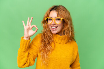 Young caucasian woman isolated on green screen chroma key background With glasses and doing OK sign