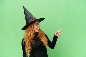 Young caucasian woman costume as witch isolated on green screen chroma key background pointing finger to the side and presenting a product