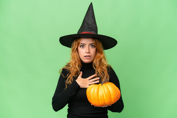 Young caucasian woman costume as witch holding a pumpkin isolated on green screen chroma key background surprised and shocked while looking right