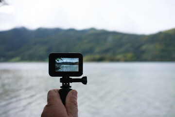 human hand holding action camera in front of scenic lake view