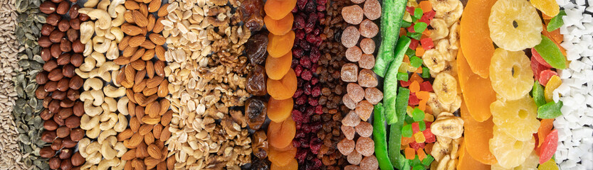 Food horizontal banner with a healthy snack. Candied fruits, dried berries, nuts, seeds on a dark background top view. Vegetarian mix of vitamin food