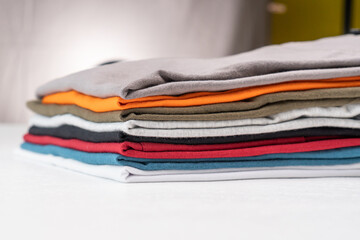 Collection of colorful plain t-shirts is stacked on the table.