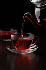 Filling a glass cup with tea from a glass teapot on a black background. Selective focus.